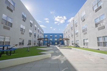 An exterior view of an apartment building with grass and benches